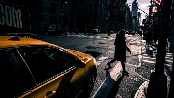 A pedestrian crosses the street in front of a yellow taxi cab.