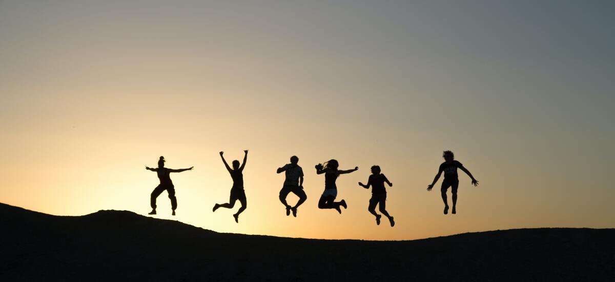 Mehrere junge Menschen stehen bei Sonnenuntergang auf einem Hügel und springen in die Luft