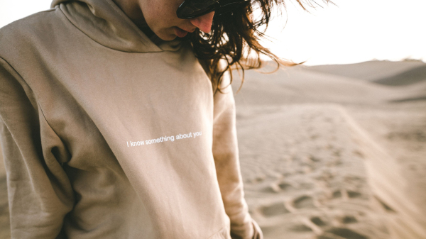 Frau in einem Pullover und mit Sonnenbrille am Strand schaut auf den Boden