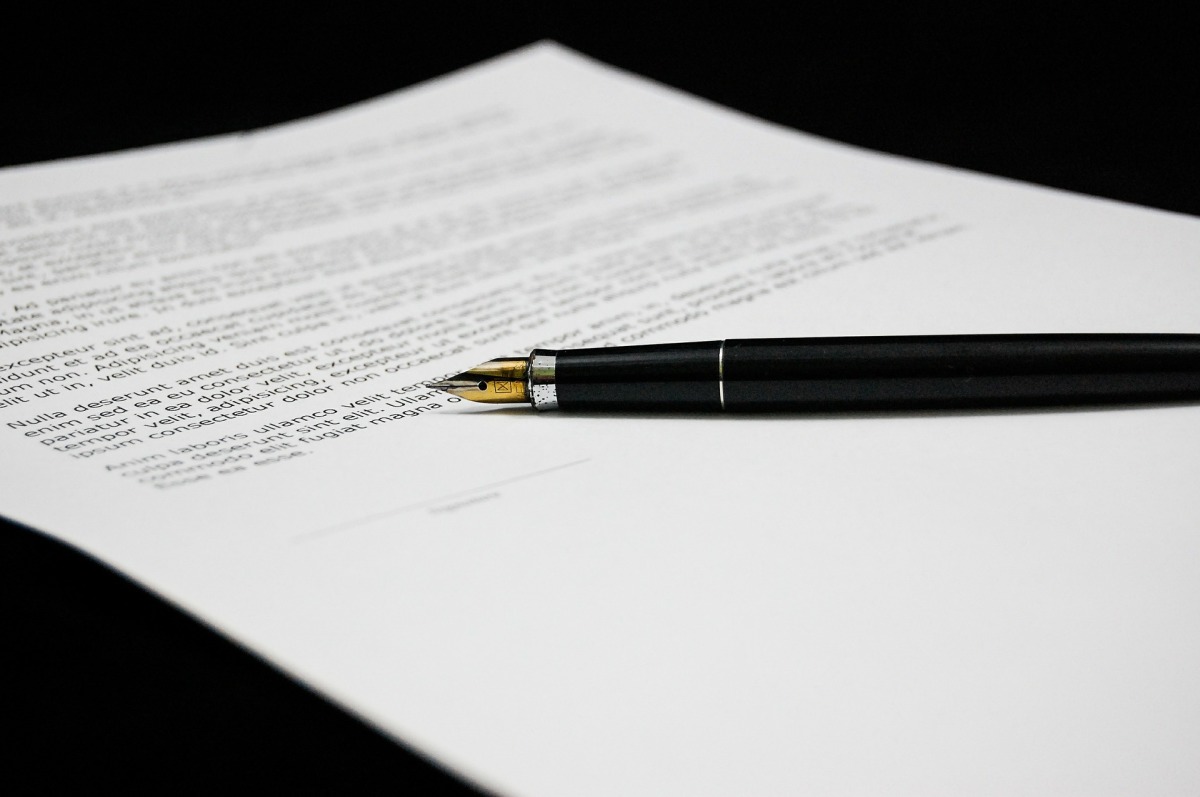Zu sehen ist ein Dokument auf einem schwarzen Tisch. Ein verzierter, geöffneter Füller liegt daneben.