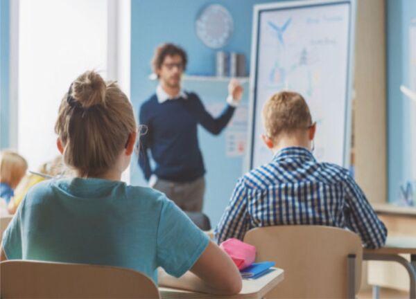eine Lehr zeigt einer Schulklasse etwas an der Tafel.
