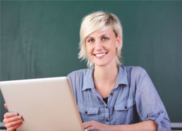Eine Frau die vor einer Tafel an einem Laptop sitzt.