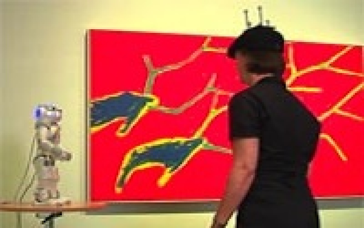 Eine Person schaut auf einen Roboter, der neben einem Gemälde steht.