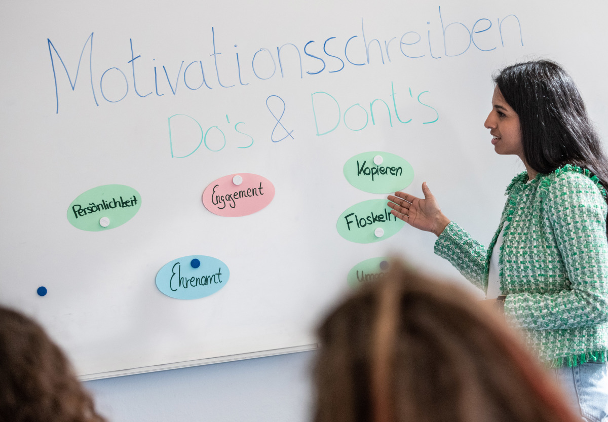 Eine Frau steht vor einem Whiteboard, auf dem "Motivationsschreiben: Dos & Don'ts steht" und erklärt etwas.
