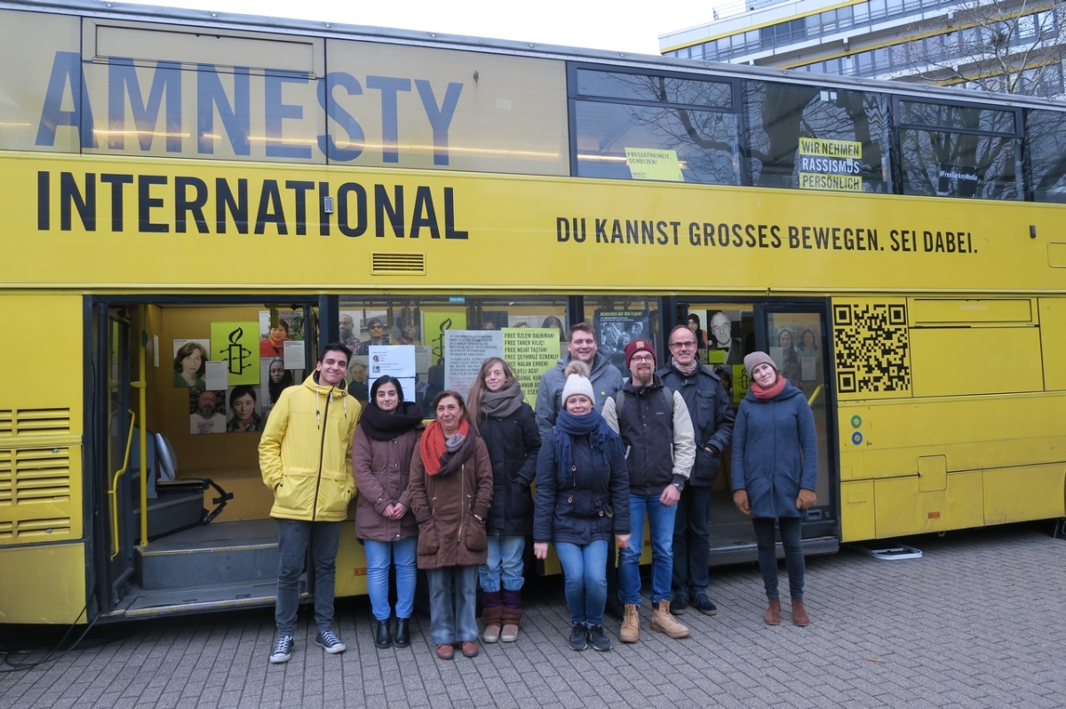 Die Amnesty-gruppe steht vor einem gelben Bus