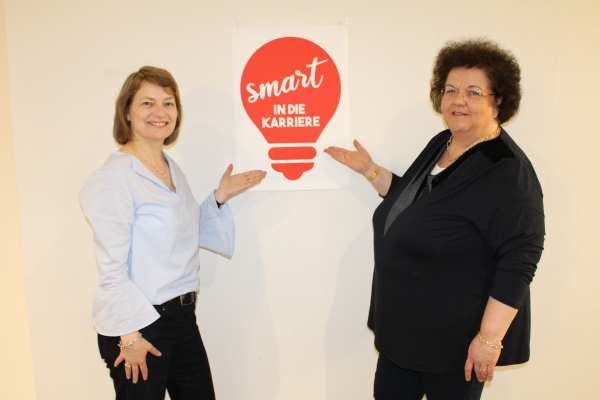 Zwei Frauen zeigen auf ein Schild, auf dem 