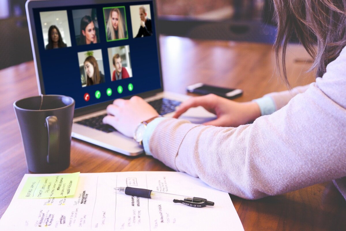 Ein Bild von einer Person mit Laptop, auf dem eine Videokonferenz zu sehen ist