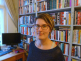 Portrait showing Dr. Maria Sulimma in front of a book shelf and a computer screen.
