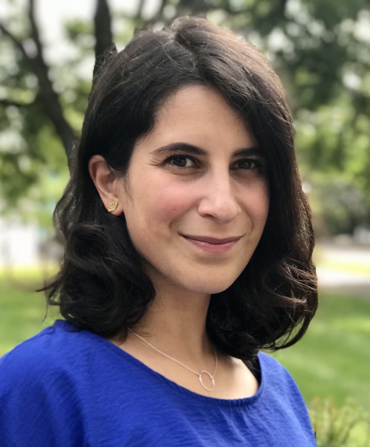 Portrait of a brown woman in front of a blurred, tree-filled background