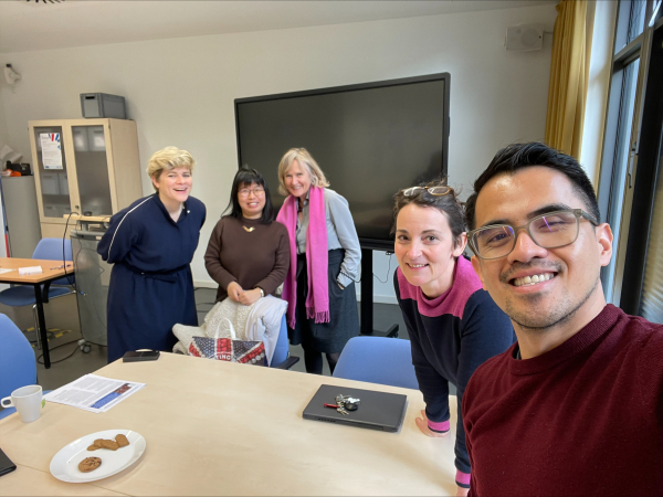 Selfie of a white woman with blonde hair, an Asian woman with black hair, an older white woman wearing a pink scarf, a white woman with glasses on her head, and an Asian man with glasses