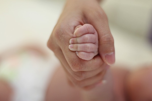 Eine vermutlich weibliche Hand hält die Hand eines babys