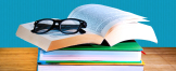 Eine Hornbrille liegt auf einem Stapel Bücher, von denen eins aufgeschlagen ist.