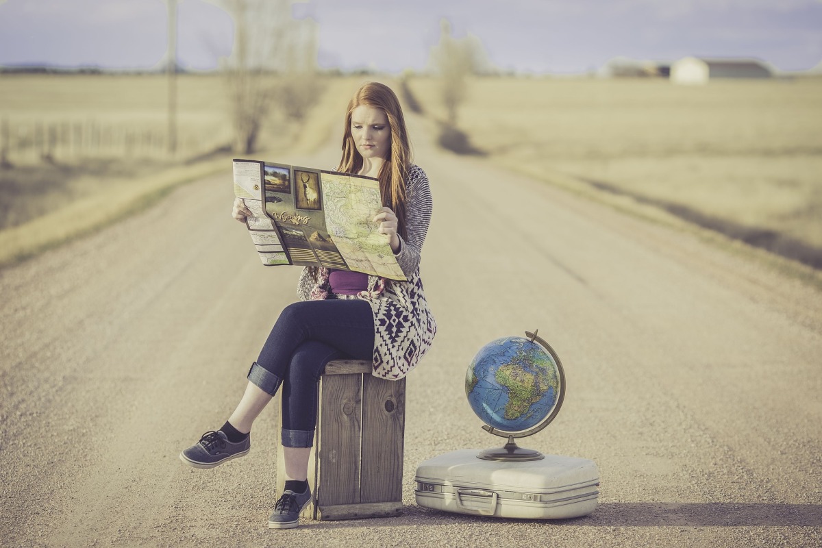 Frau sitzt auf einem Koffer und schaut in eine Landkarte