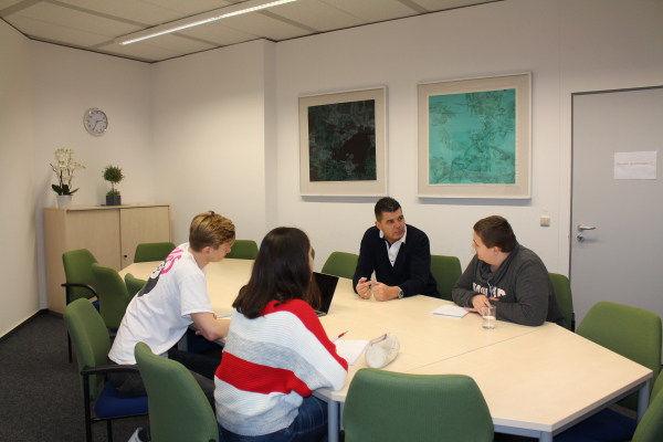 Das Foto zeigt die Gruppenarbeit von Studierenden im Gespräch mit dem Dozenten