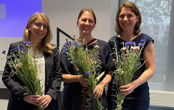 Melitta Gillmann, Judith Purkarthofer und Eva Gredel vor der Bühne des Glaspavillons, mit Blumensträußen in den Händen