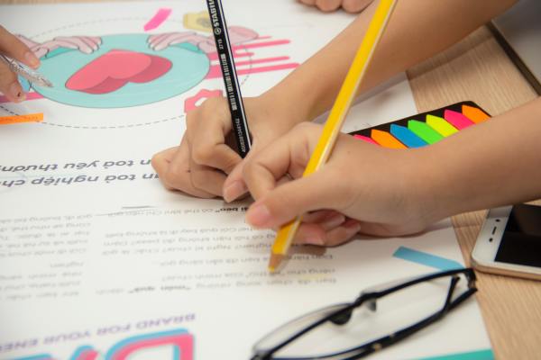 2 Kinderhände schreiben mit Buntstiften auf ein bedrucktes Plakat