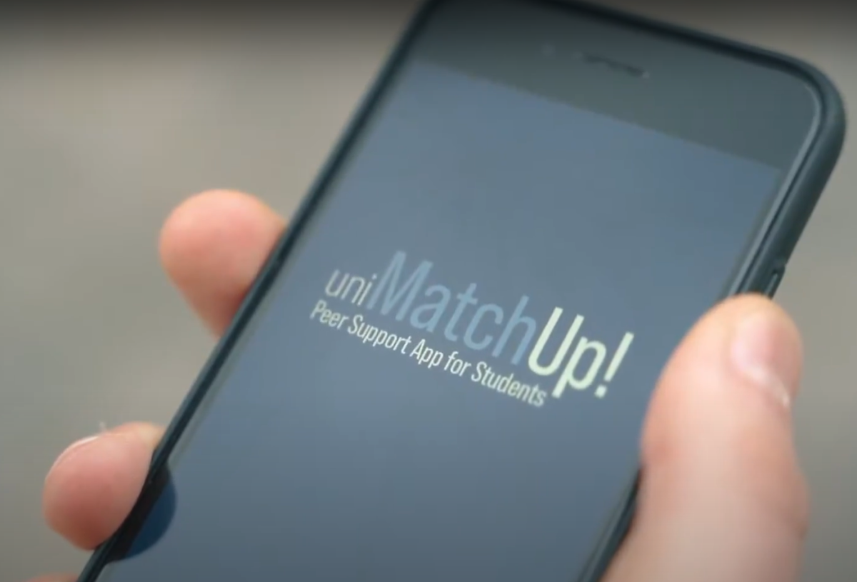 Ein Smartphone, das jemand in der Hand hält und auf dem der Titel "uniMatchUp! Peer Support App for Students" zu sehen ist.