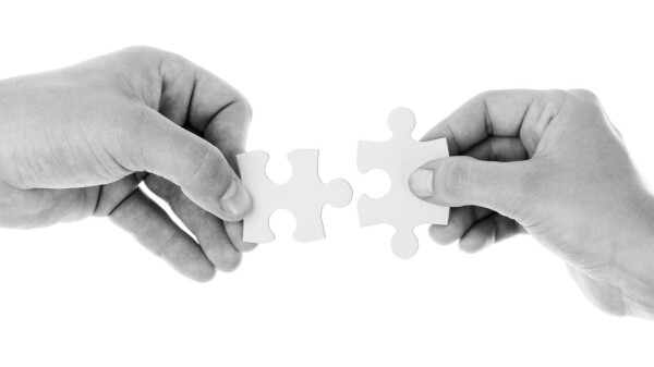 Zwei Hände, die zwei Puzzle-Stücke zusammenführen