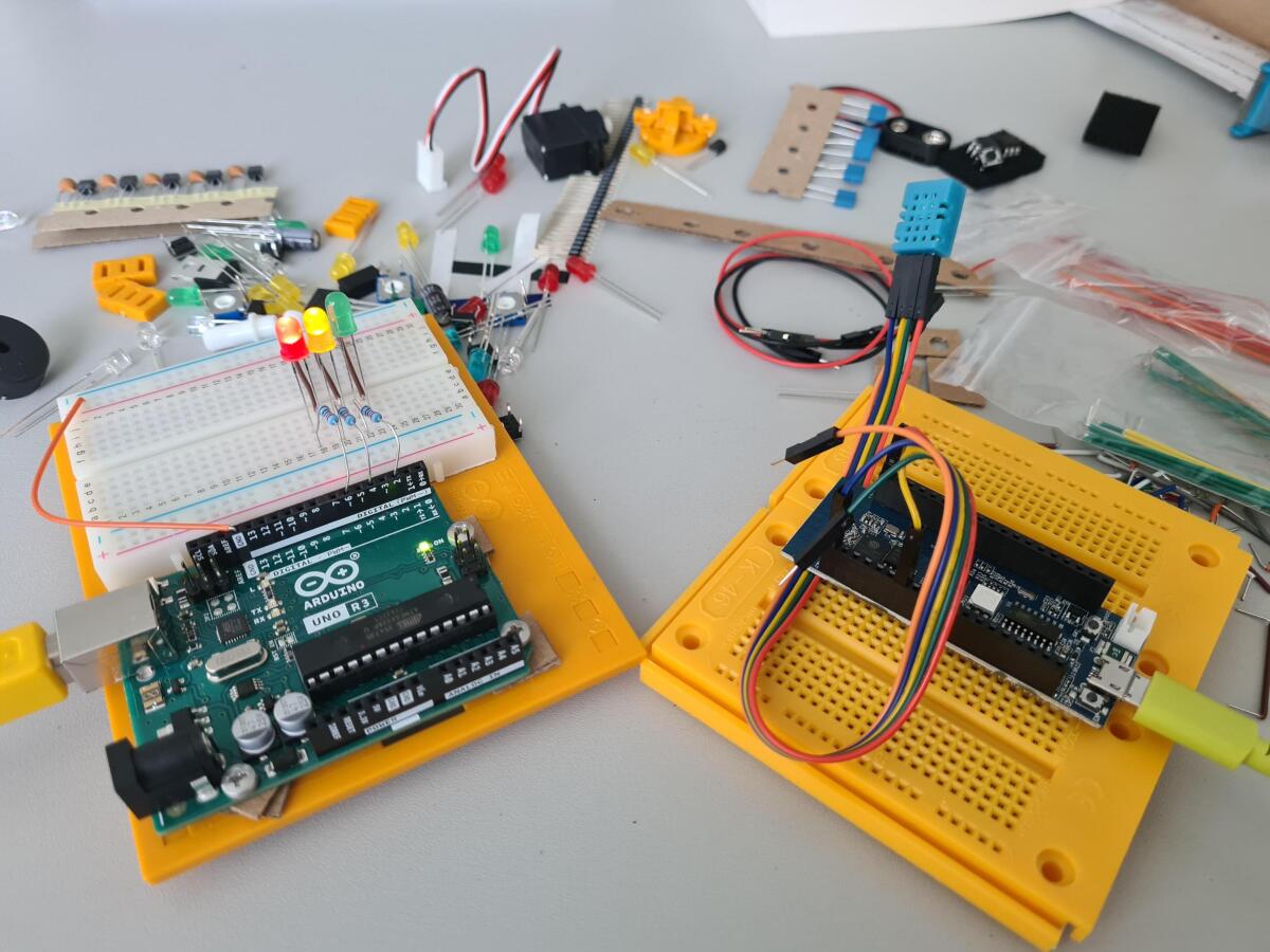 Auf dem Tisch liegen viele Elektronische Bauteile, im Vordergrund sind zwei Microcontroller mit Schaltungen aufgebaut.