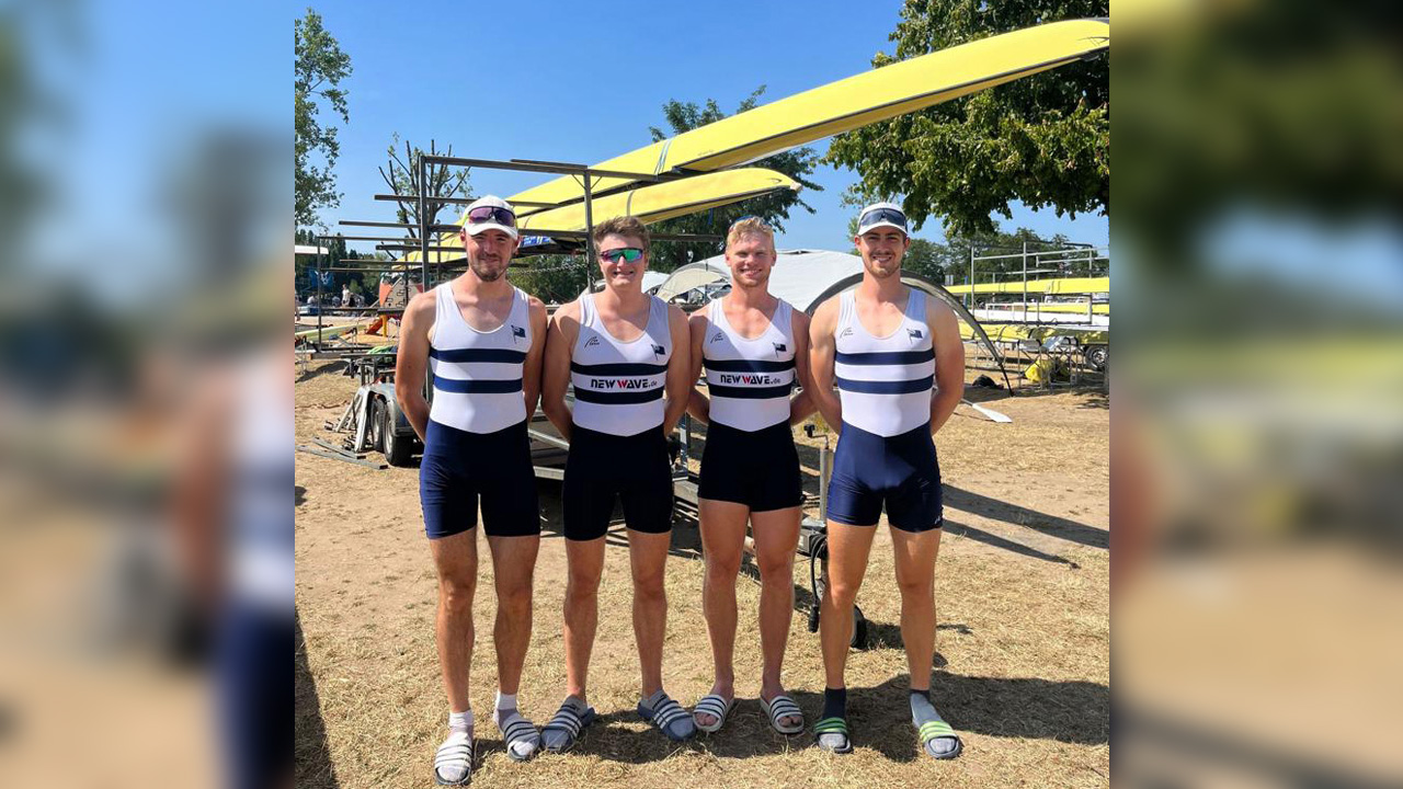 Gruppenbild des Ruderteams.Vier Männer, im Hintergrund zwei Kanus auf einem Gestell