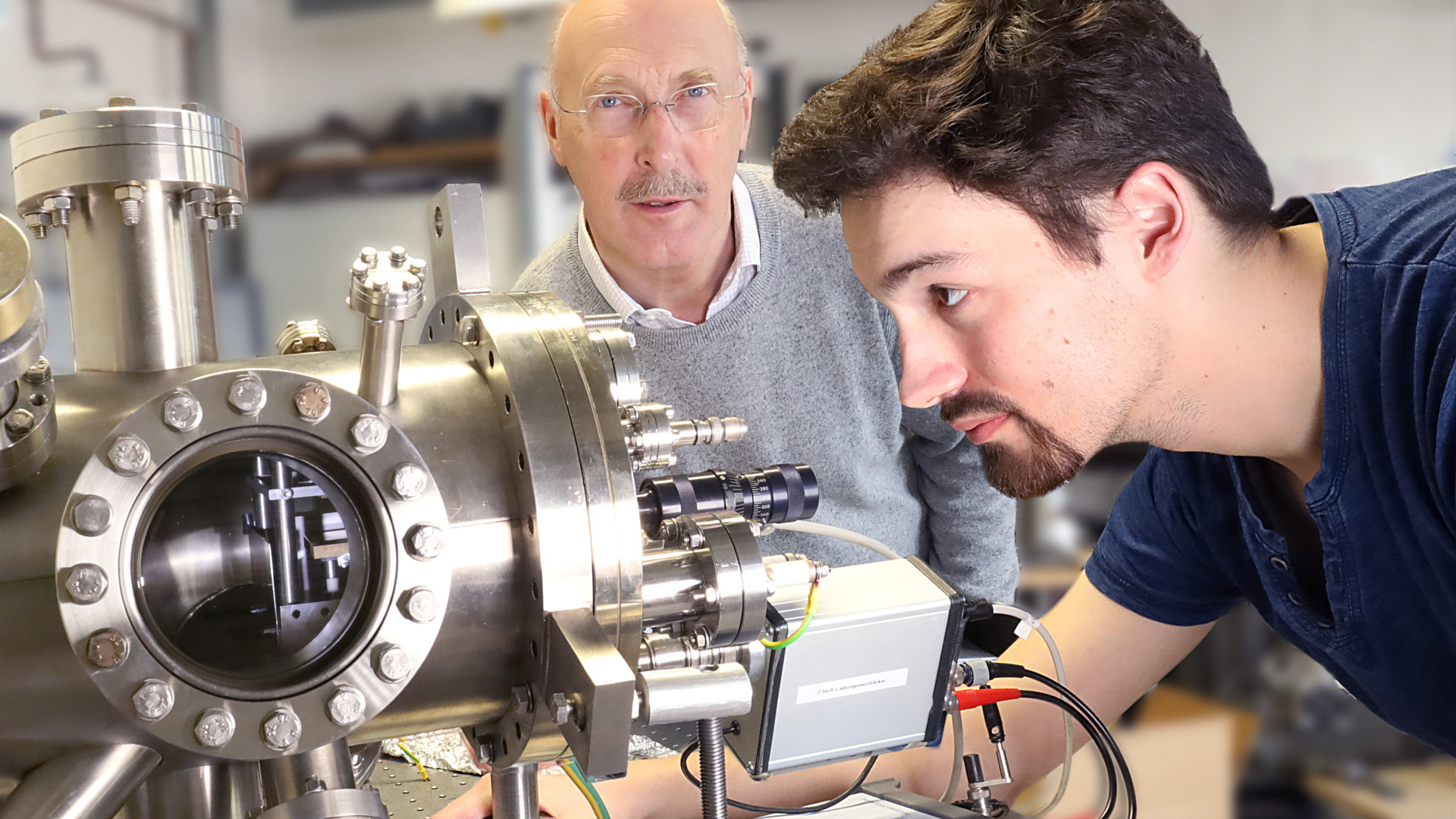 Andre Mölleken schaut auf den röhrenförmigen Aufbau des Experiments. Professor Möller sieht darüber hinweg in die Kamera.