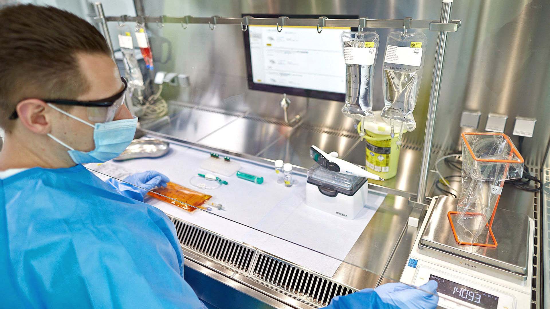 Ein Mann im blauen Kittel und mit Mundschutz sowie Schutzbrille im Labor