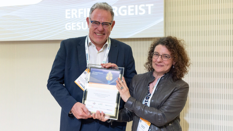 Foto: Zwei Personen, die eine Urkunde halten. Links ist Prof. Giebel zu sehen, neben ihm Dr. Angelika Vlachou. Beide lächeln in die Kamera.