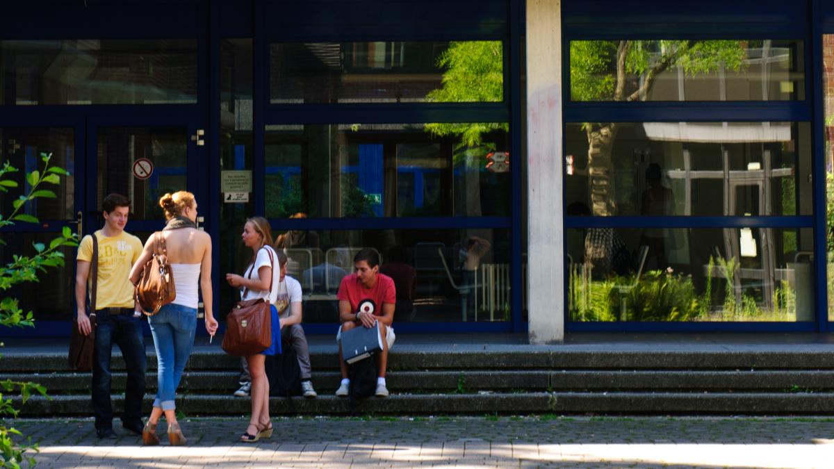 Auf dem Bild sieht man eine Gruppe von Personen, die sich vor einem Gebäude der Universität Duisburg-Essen austauschen