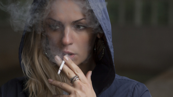 junge Frau mit Kapuze eines dunklen Hoodies auf dem Kopf, rauchend