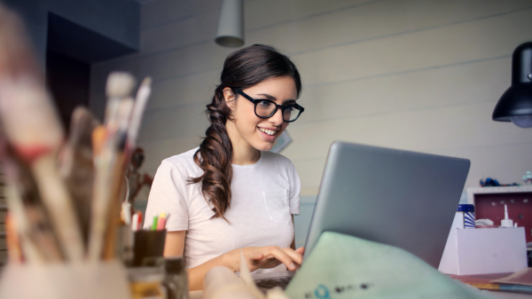 Eine junge Frau mit Brille sitzt vor einem aufgeklappten Notebook. 