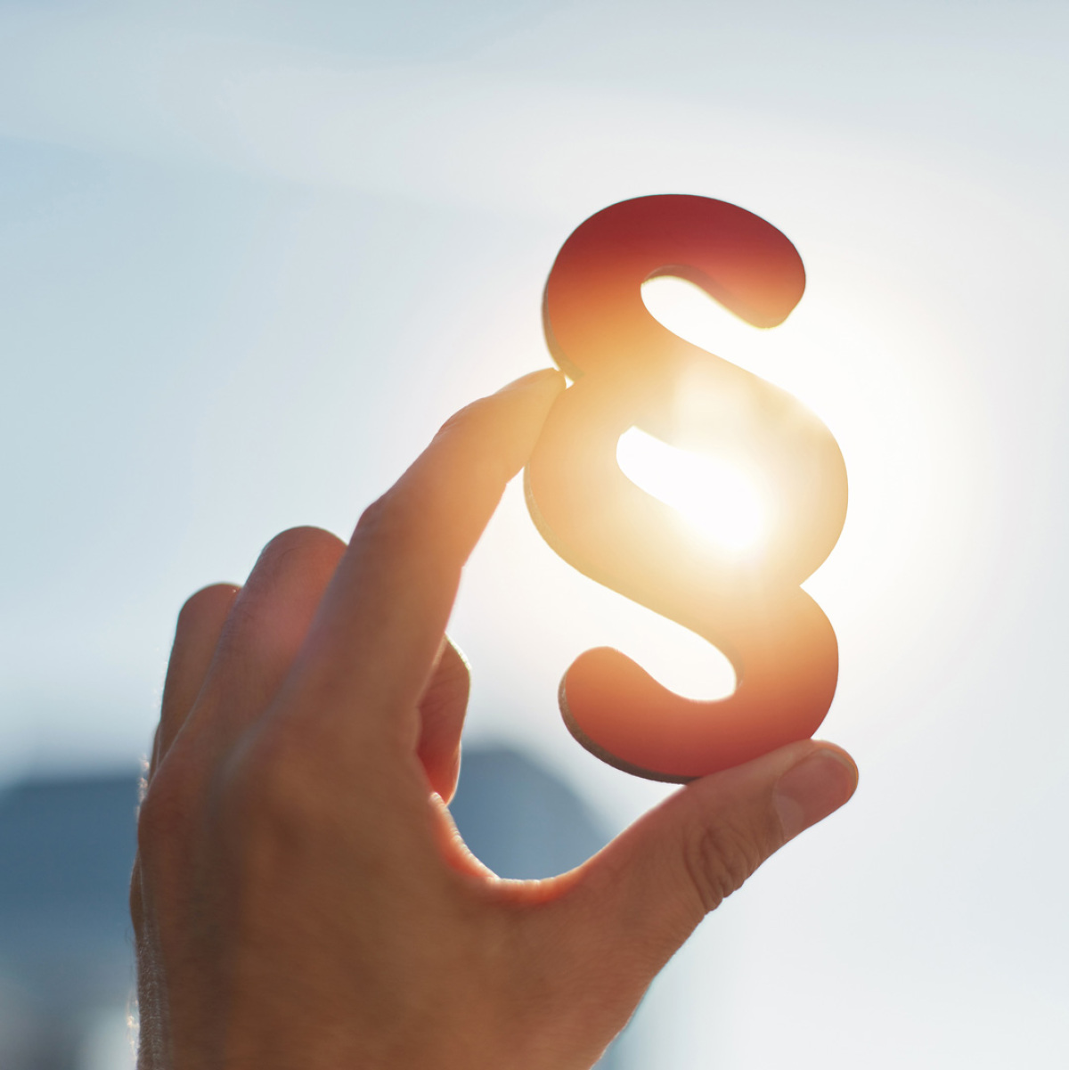 Eine Hand hält ein Paragraphen-Symbol in die Sonne.