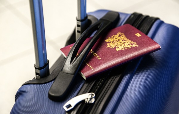 (Symbolbild) Ein blauer Koffer mit einem roten Pass, der unter den Träger geklemmt ist.