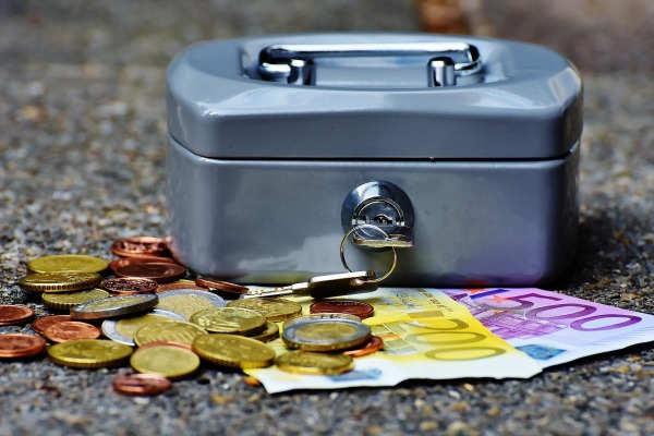 (Symbolbild) Eine silberne Gerldkassette steht auf der Straße. Unter ihr liegt Kleingeld und je ein 500€-Schein und ein 200€-Schein.